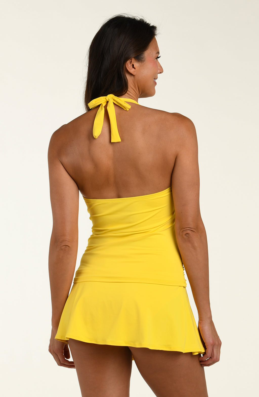 Woman wearing a yellow tankini top and matching swim skirt against a white background. 