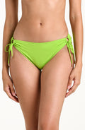 Woman wearing an apple green side tie hipster bikini bottom against a white background.