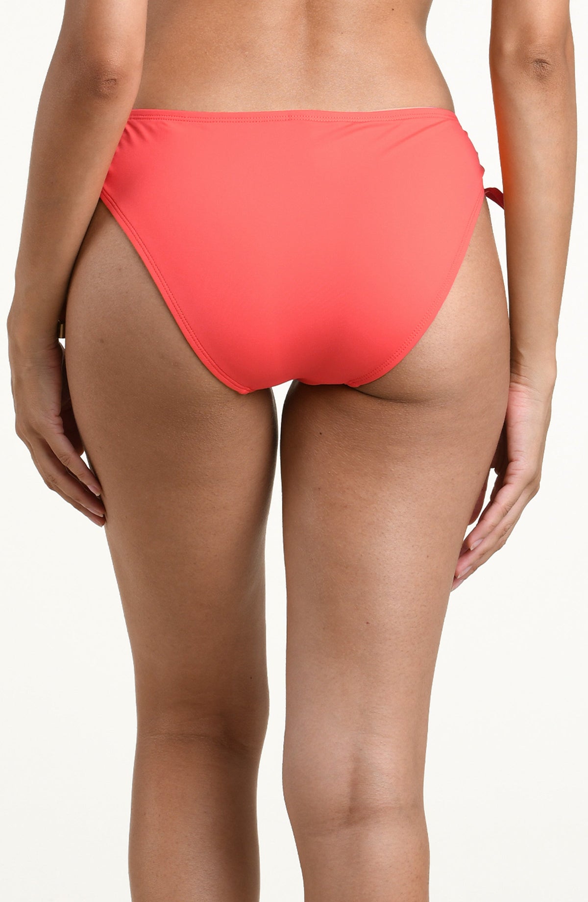 Woman wearing a bright orange bikini bottom with side ties against a white background. 