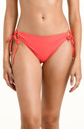 Woman wearing a bright orange bikini bottom with side ties against a white background. 