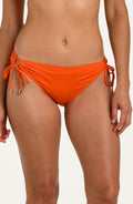 Front image of model wearing a tangelo (orange) colored bikini bottoms with adjustable side ties accented with gold tips.