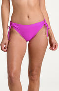 Woman wearing violet colored side tie bikini bottoms against a white background. 