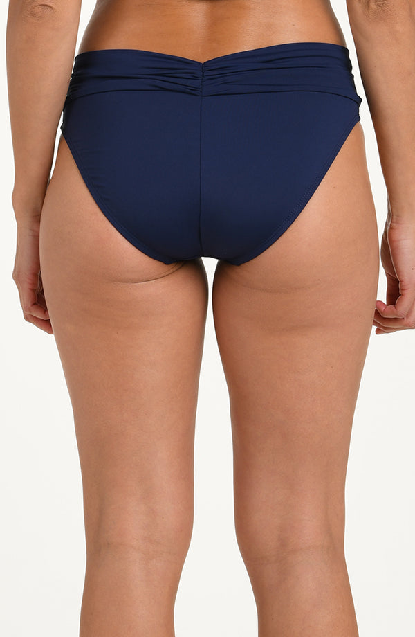 Back image of model wearing an indigo (navy blue) colored bikini bottoms with a wide, ruched waistband and moderate rear coverage.