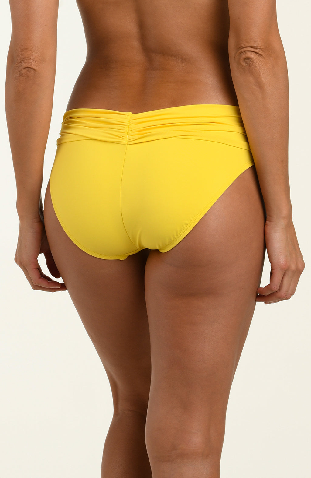 Woman wearing yellow bikini bottoms against a white background.