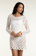 A woman modeling a white long-sleeve crochet mini dress with a scalloped hem against a plain light background.