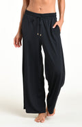 Woman wearing solid black beach pants against a white background. 