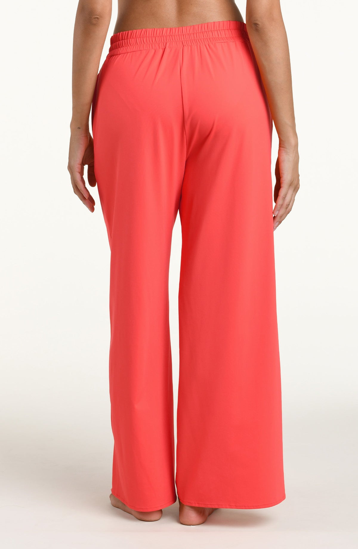 Woman wearing bright orange beach pants against a white background. 