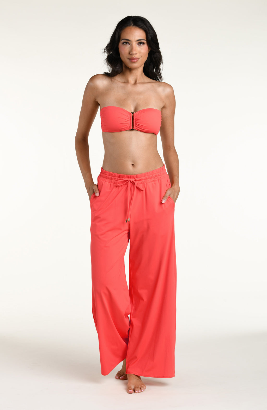 Woman wearing a bright orange bandeau bikini top and matching beach pants against a white background. 