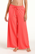 Woman wearing bright orange beach pants against a white background. 