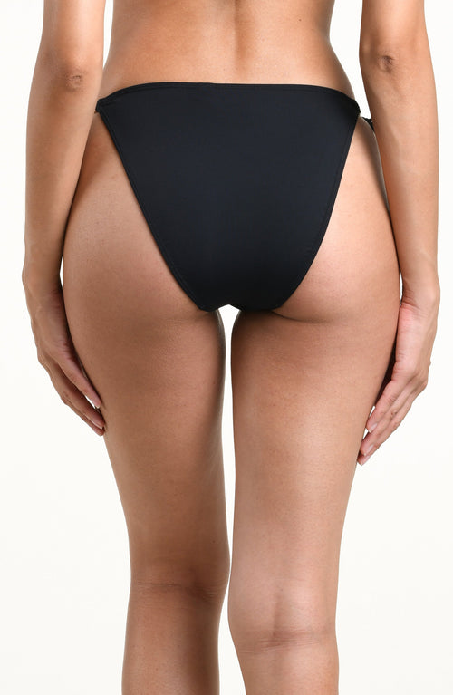 Woman wearing a solid black bikini bottom with side ties against a white background. 