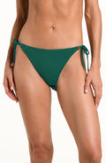 Woman wearing a solid jungle green bikini bottom with side ties against a white background.