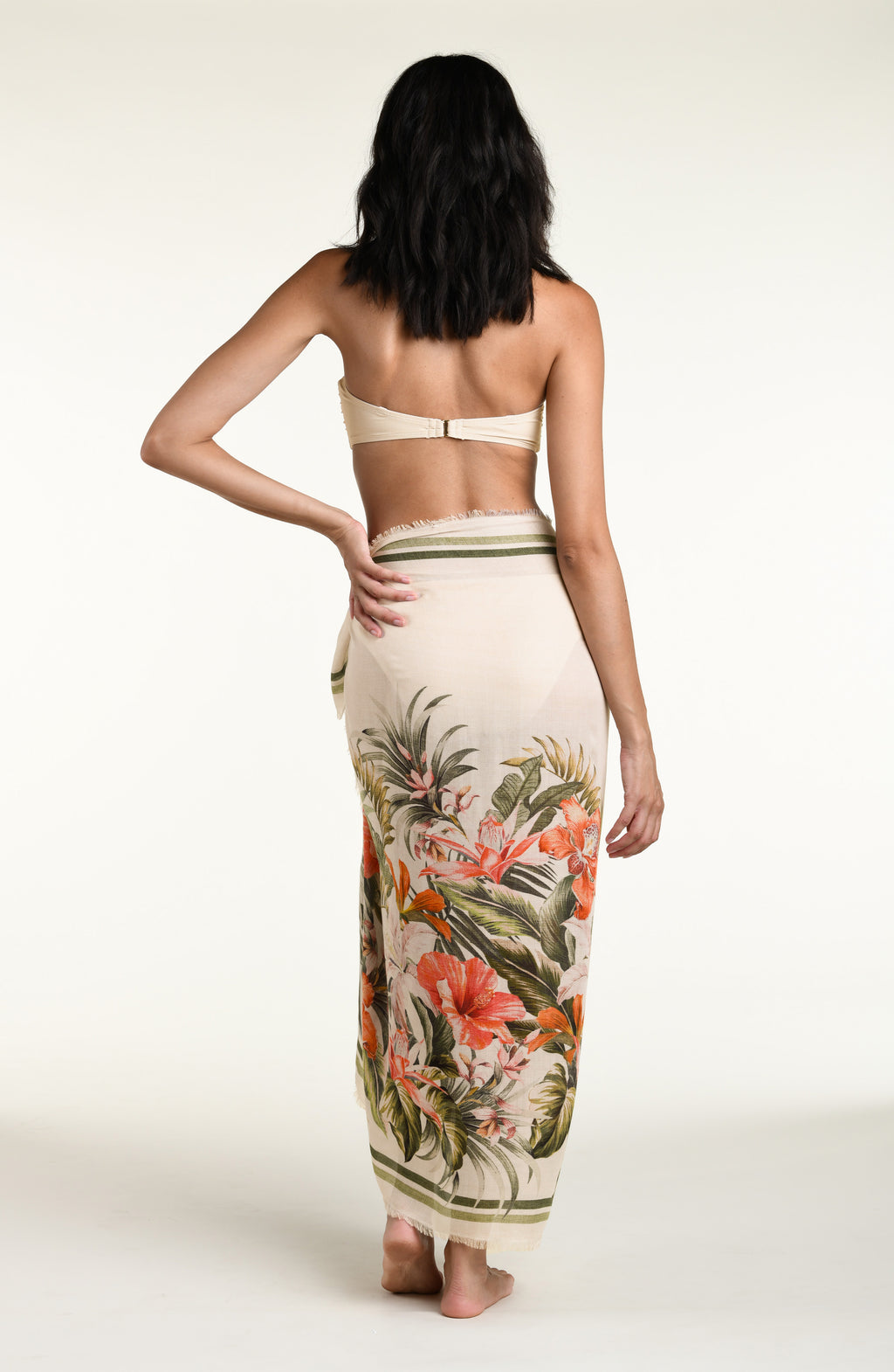 Woman wearing a white multicolored bikini top and matching pareo wrap cover up against a white background. 