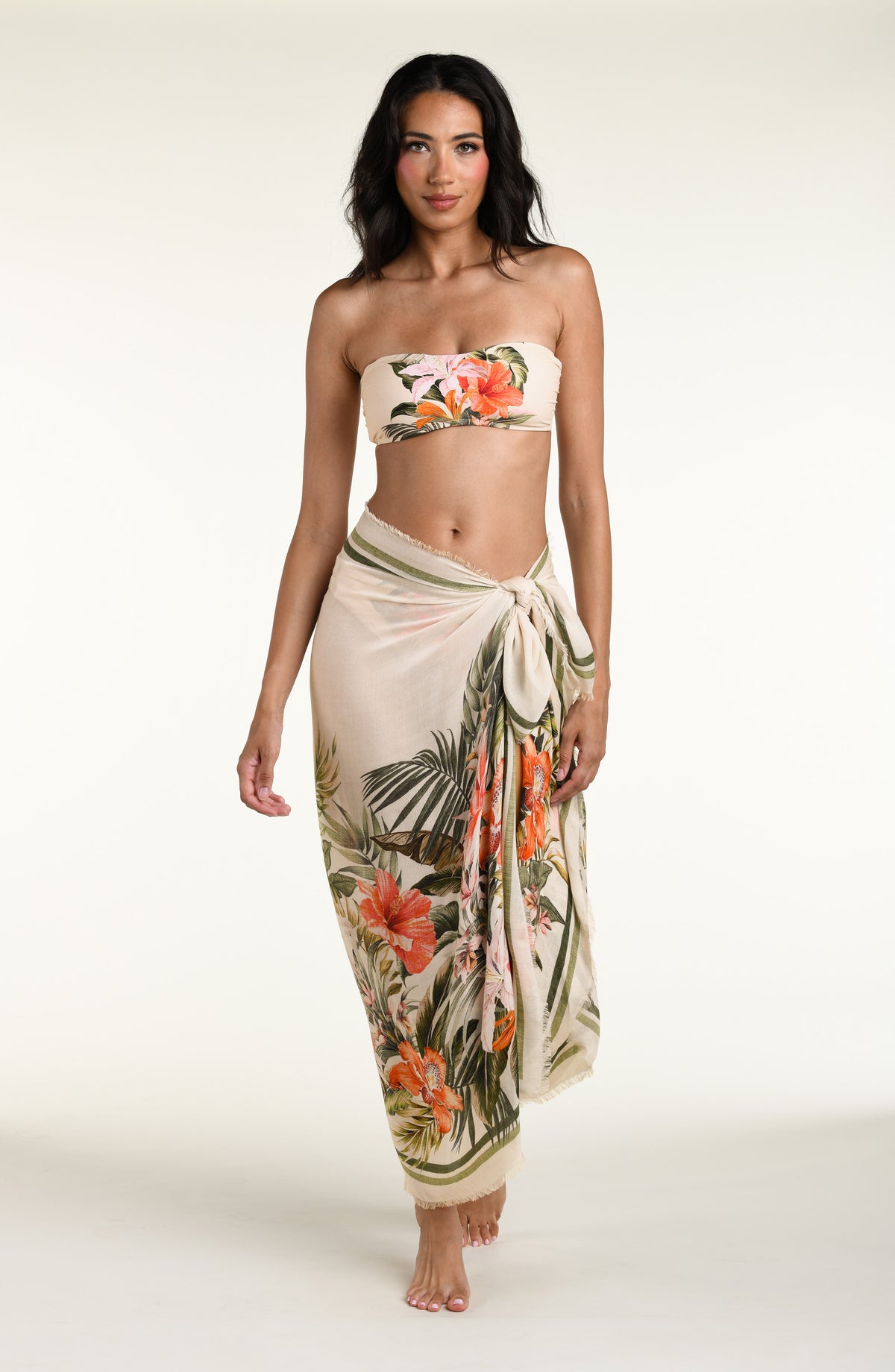 Woman wearing a white multicolored bikini top and matching pareo wrap cover up against a white background. 