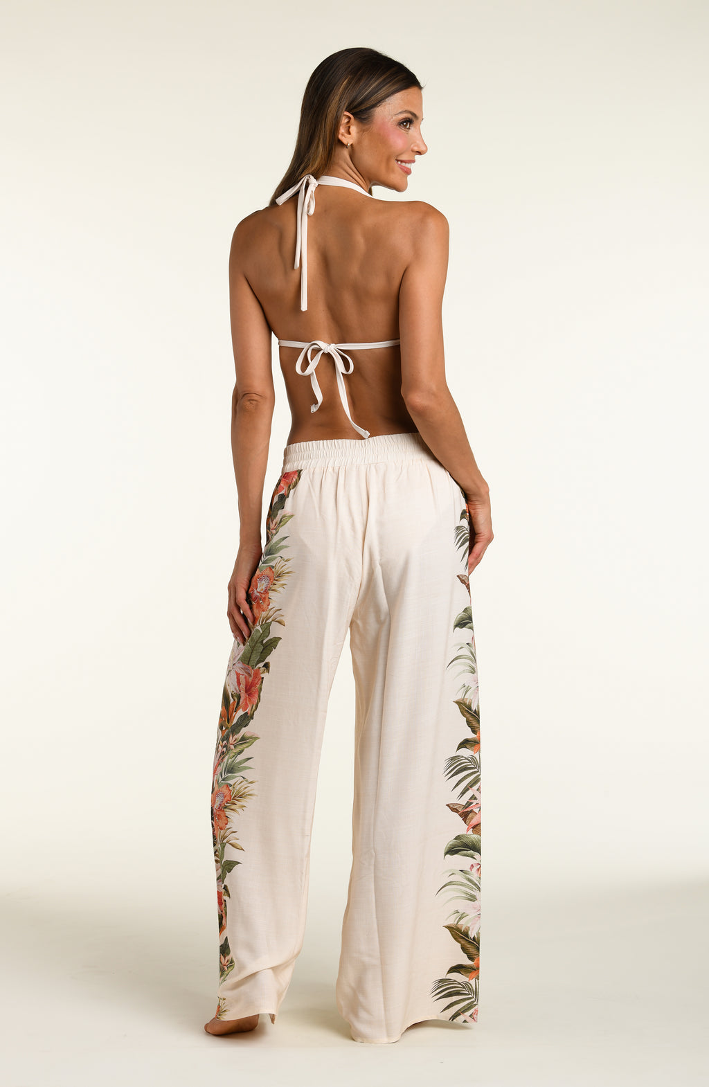 Woman wearing a white multicolored bikini top and matching pants against a white background. 
