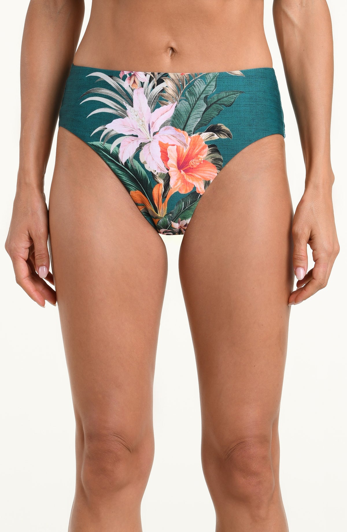 A model wearing high-waisted bikini bottoms with a tropical floral print on a teal green background, featuring pink, orange, and white flowers with green leaves.