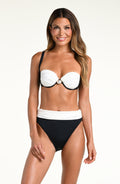 A woman modeling a two-piece bikini set against a plain light background. The bikini top is white with black trim and a small pearl-like center detail, while the bottoms are solid black with a wide white waistband.