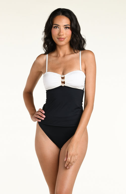 A woman wearing a black and white contrasting tankini top and black bottom against a white background. 
