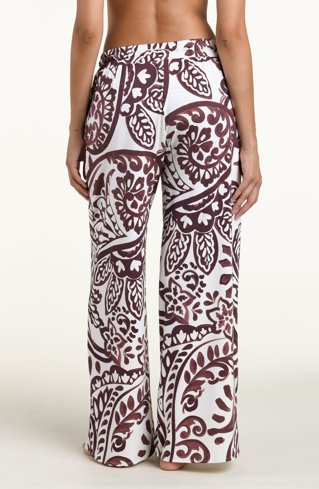 A person wearing loose, wide-leg pants with an allover paisley-style print in dark brown and white against a plain light background.