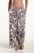 A person wearing loose, wide-leg pants with an allover paisley-style print in dark brown and white against a plain light background.
