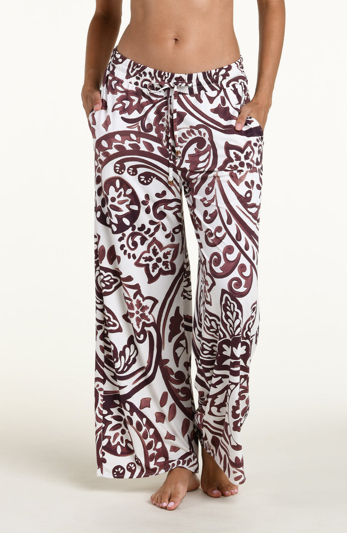 A person wearing loose, wide-leg pants with an allover paisley-style print in dark brown and white against a plain light background.