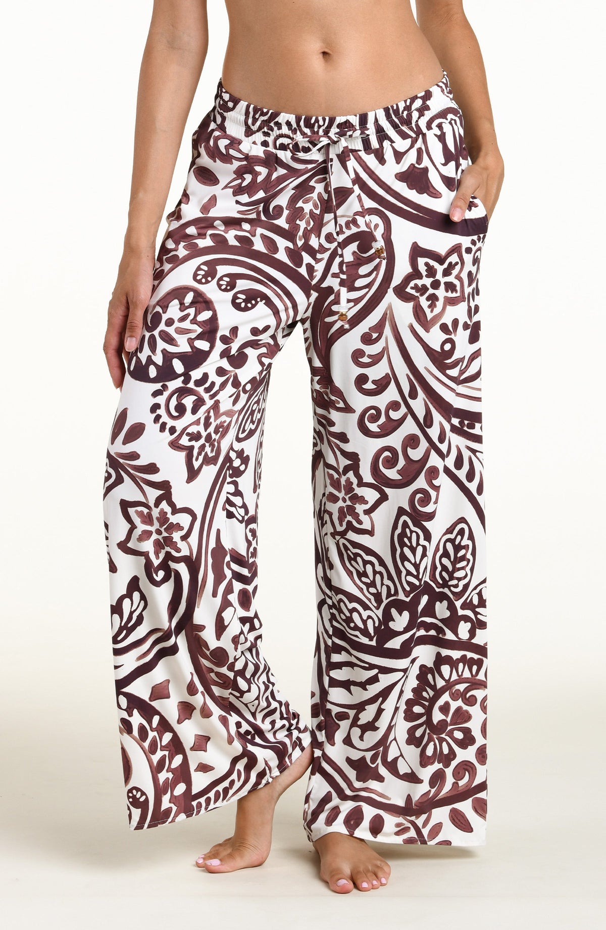 A person wearing loose, wide-leg pants with an allover paisley-style print in dark brown and white against a plain light background.