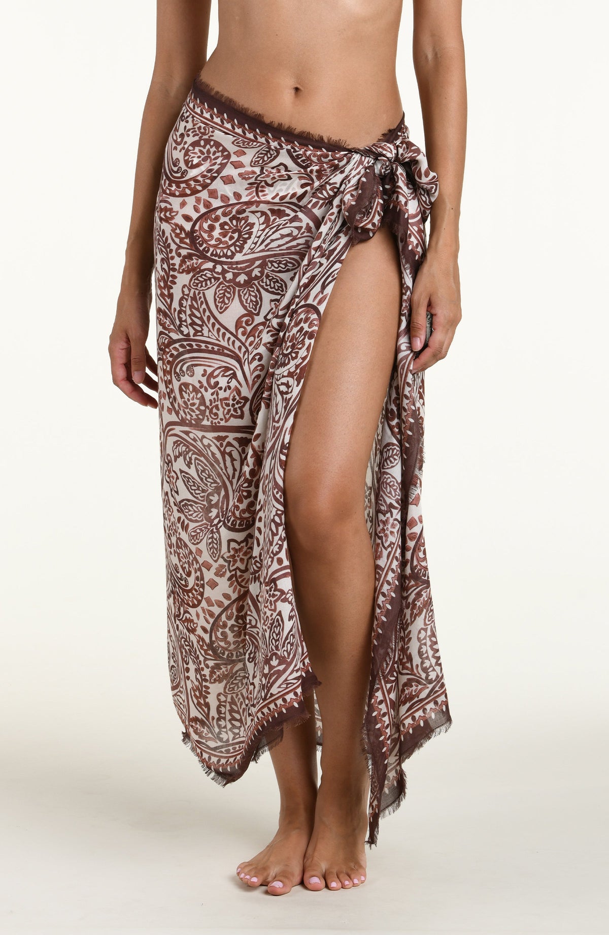 A woman wearing a brown and beige paisley-patterned sarong wrap against a plain light background.