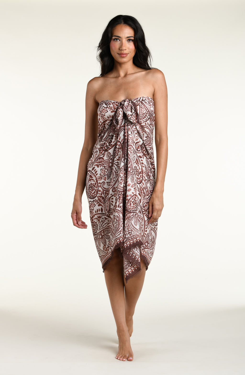 A woman wearing a brown and beige paisley-patterned sarong wrap against a plain light background.