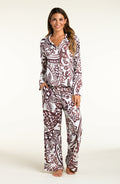 A woman modeling a matching long-sleeve button-front pajama top and wide-leg pajama pants set with an intricate paisley pattern in dark brown and white, set against a plain off-white studio background.