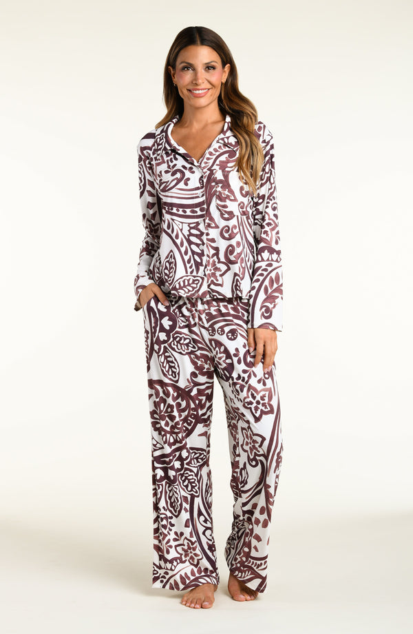 A woman modeling a matching long-sleeve button-front pajama top and wide-leg pajama pants set with an intricate paisley pattern in dark brown and white, set against a plain off-white studio background.