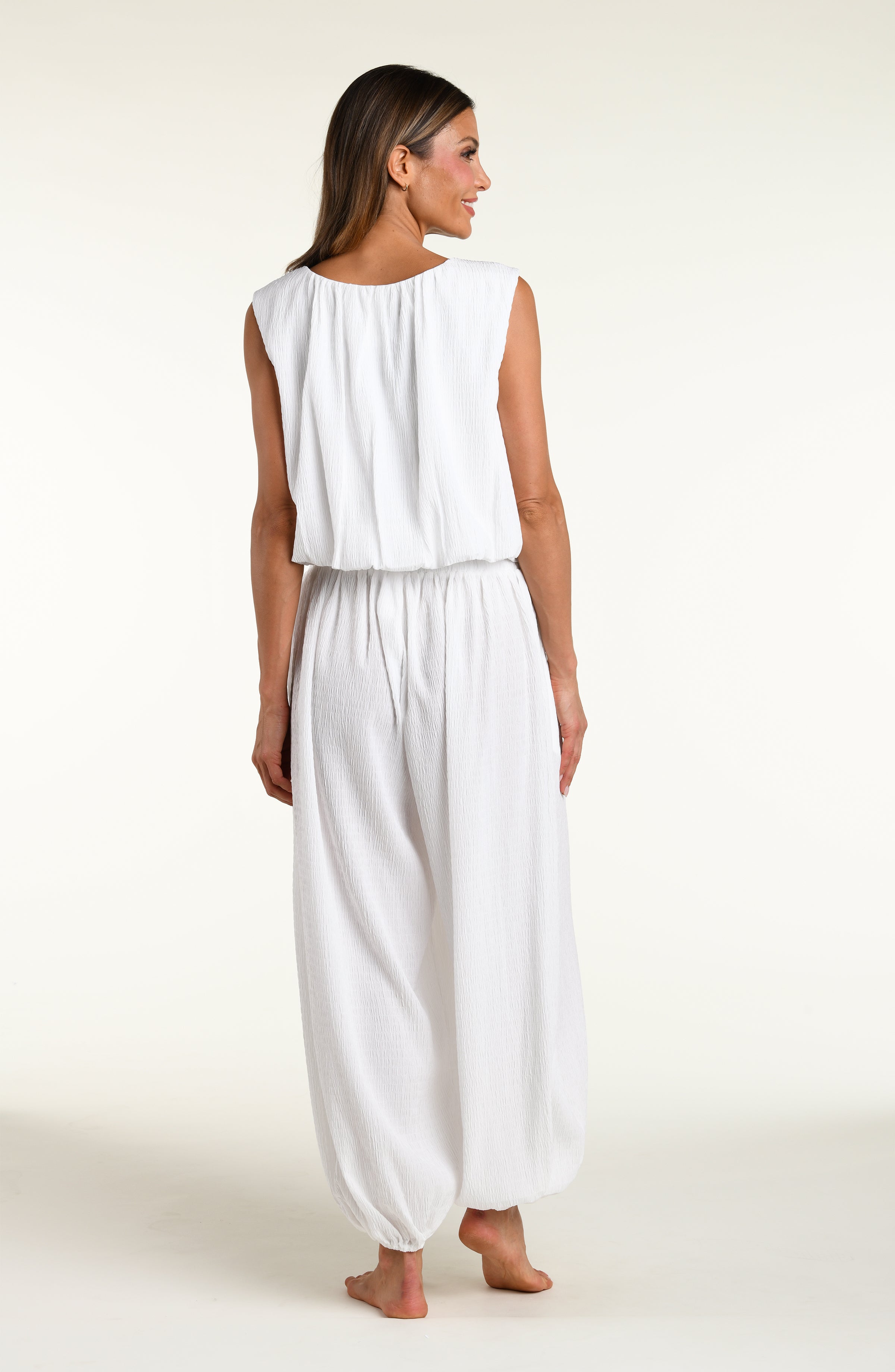 Woman wearing white crochet style beach pants and matching sleeveless top against a white background. 