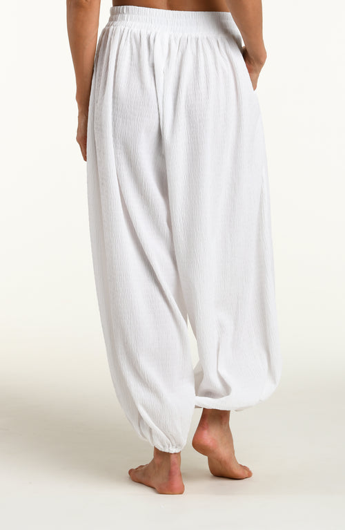 Woman wearing white crochet style beach pants against a white background. 