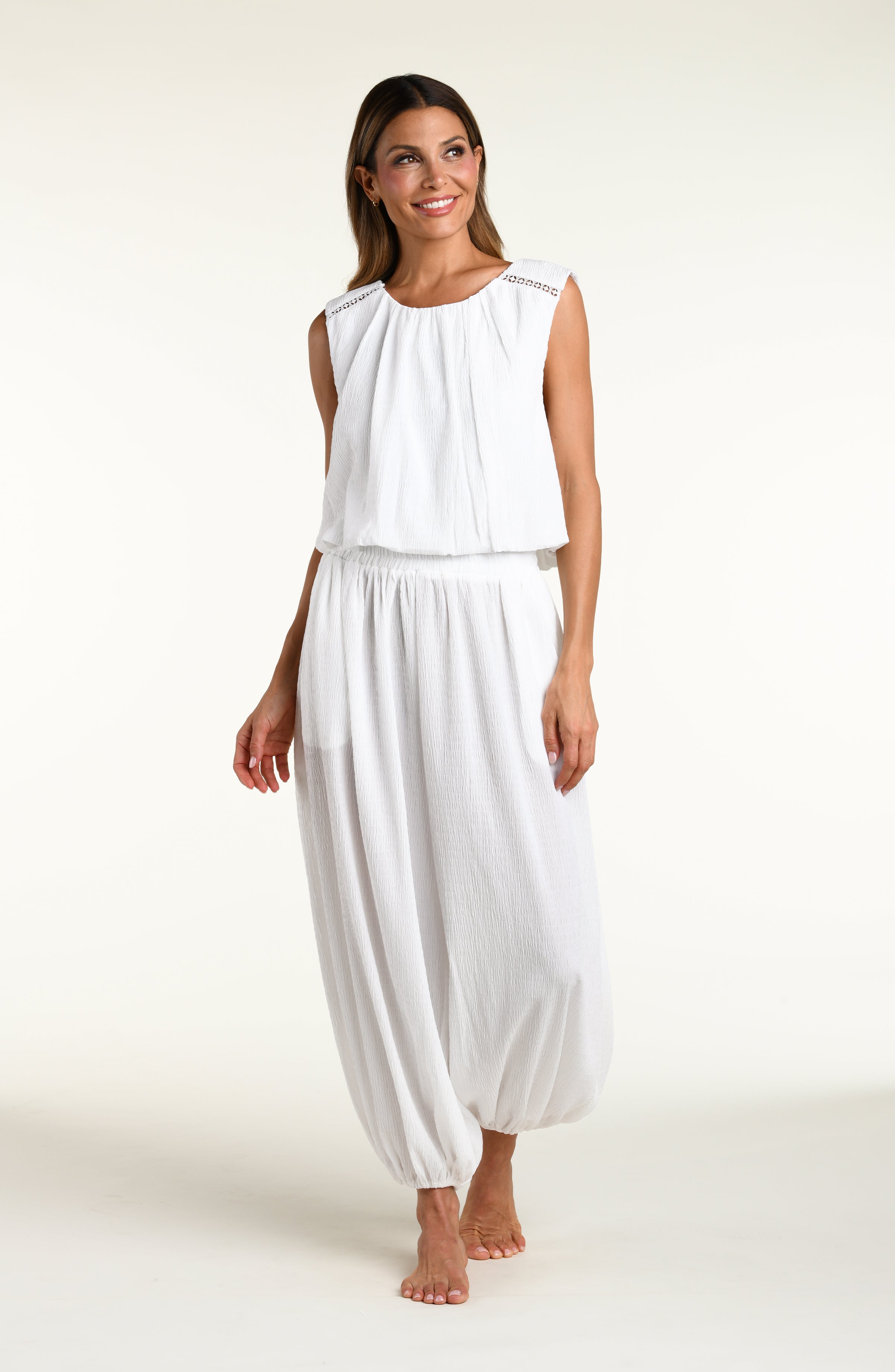Woman wearing white crochet style beach pants and matching sleeveless top against a white background. 