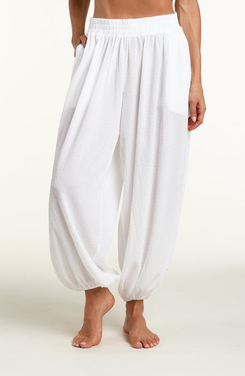 Woman wearing white crochet style beach pants against a white background. 