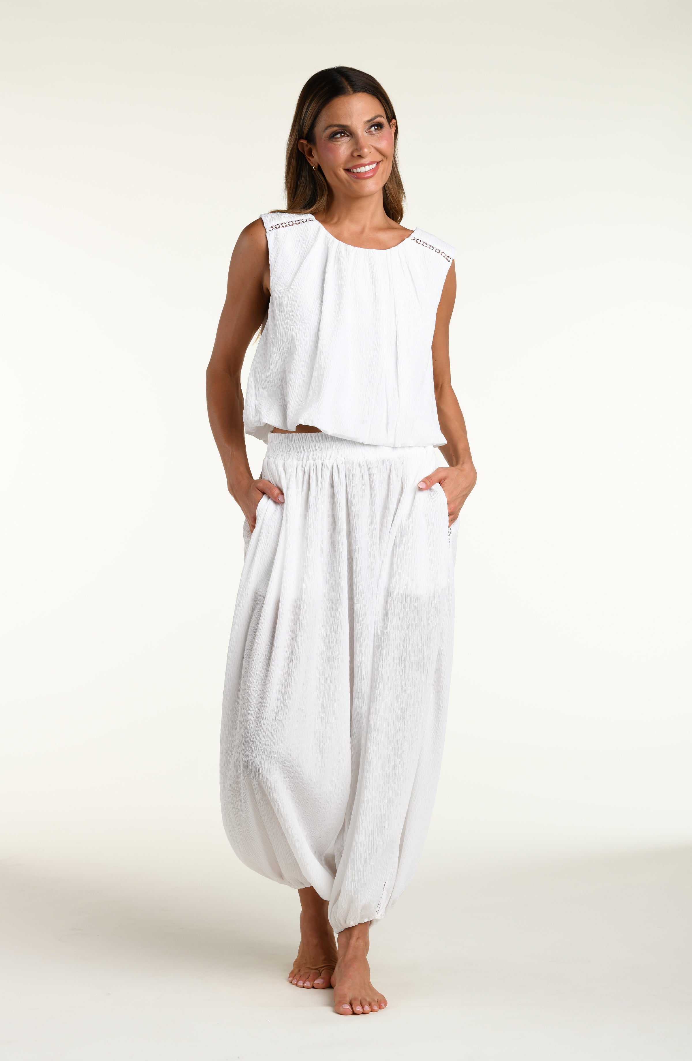 Woman wearing white crochet style beach pants and matching sleeveless top against a white background. 
