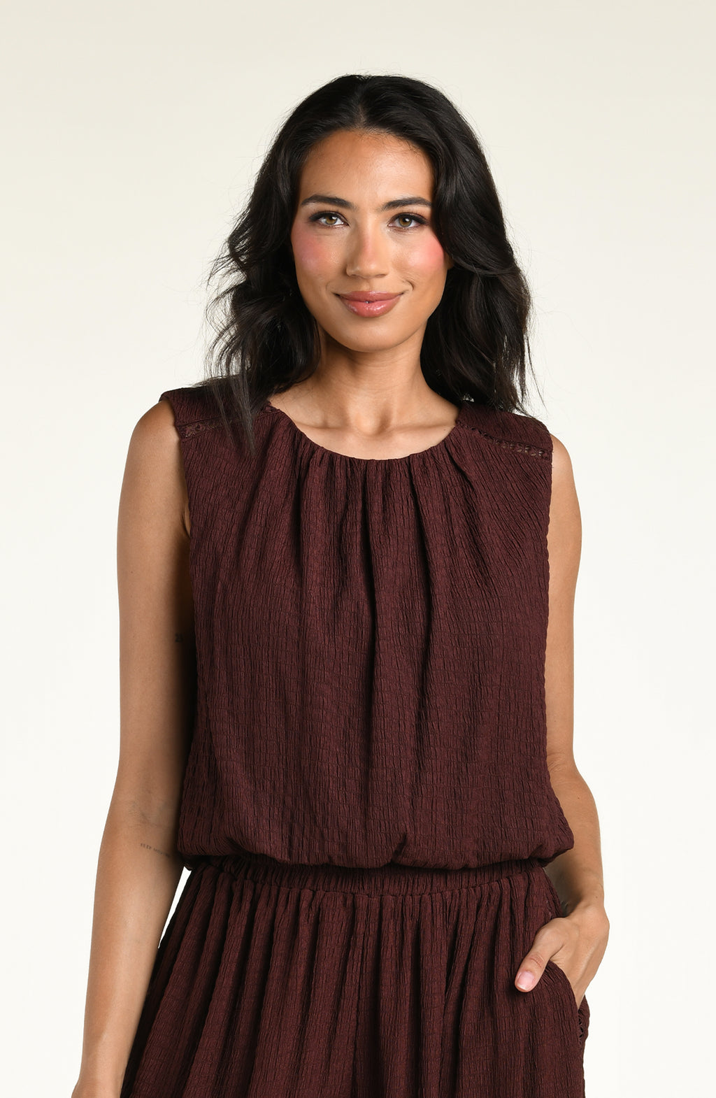 Woman wearing a java brown colored sleeveless top against a white background. 