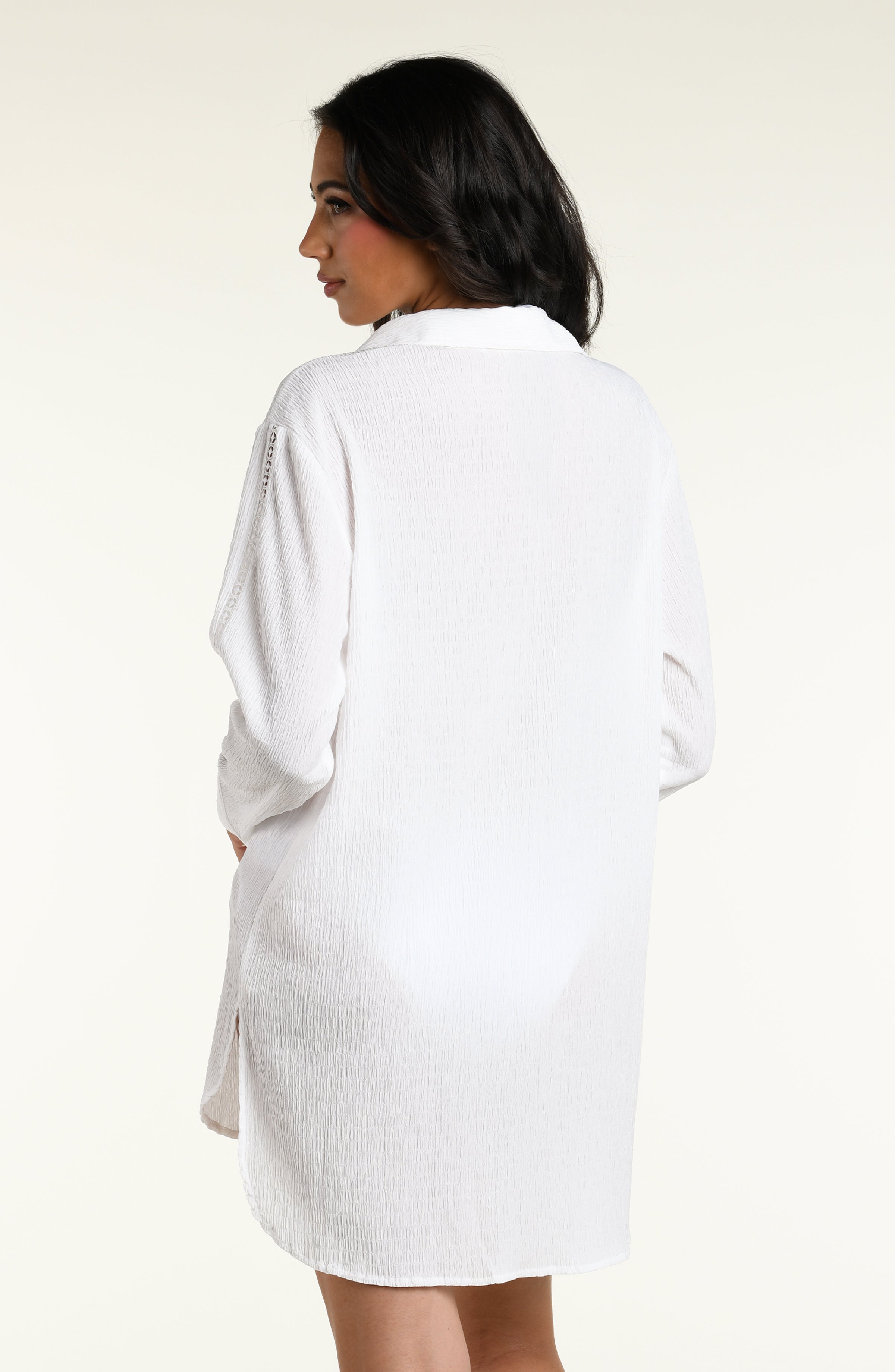 Woman wearing a white long sleeve cover up top against a white background. 