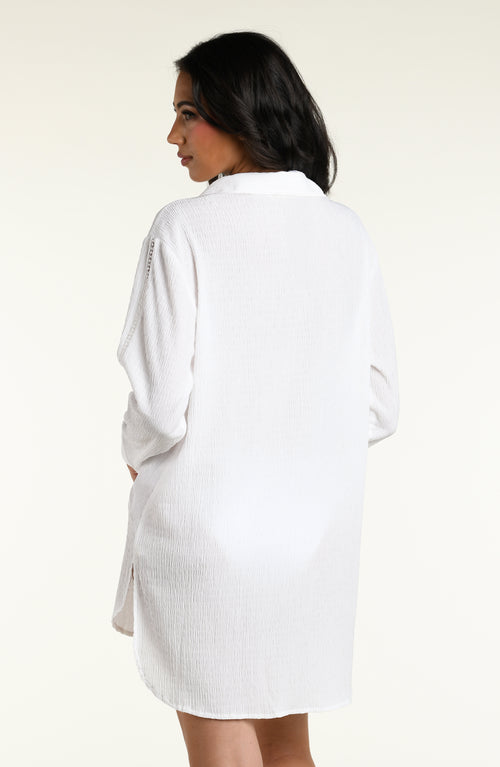 Woman wearing a white long sleeve cover up top against a white background. 