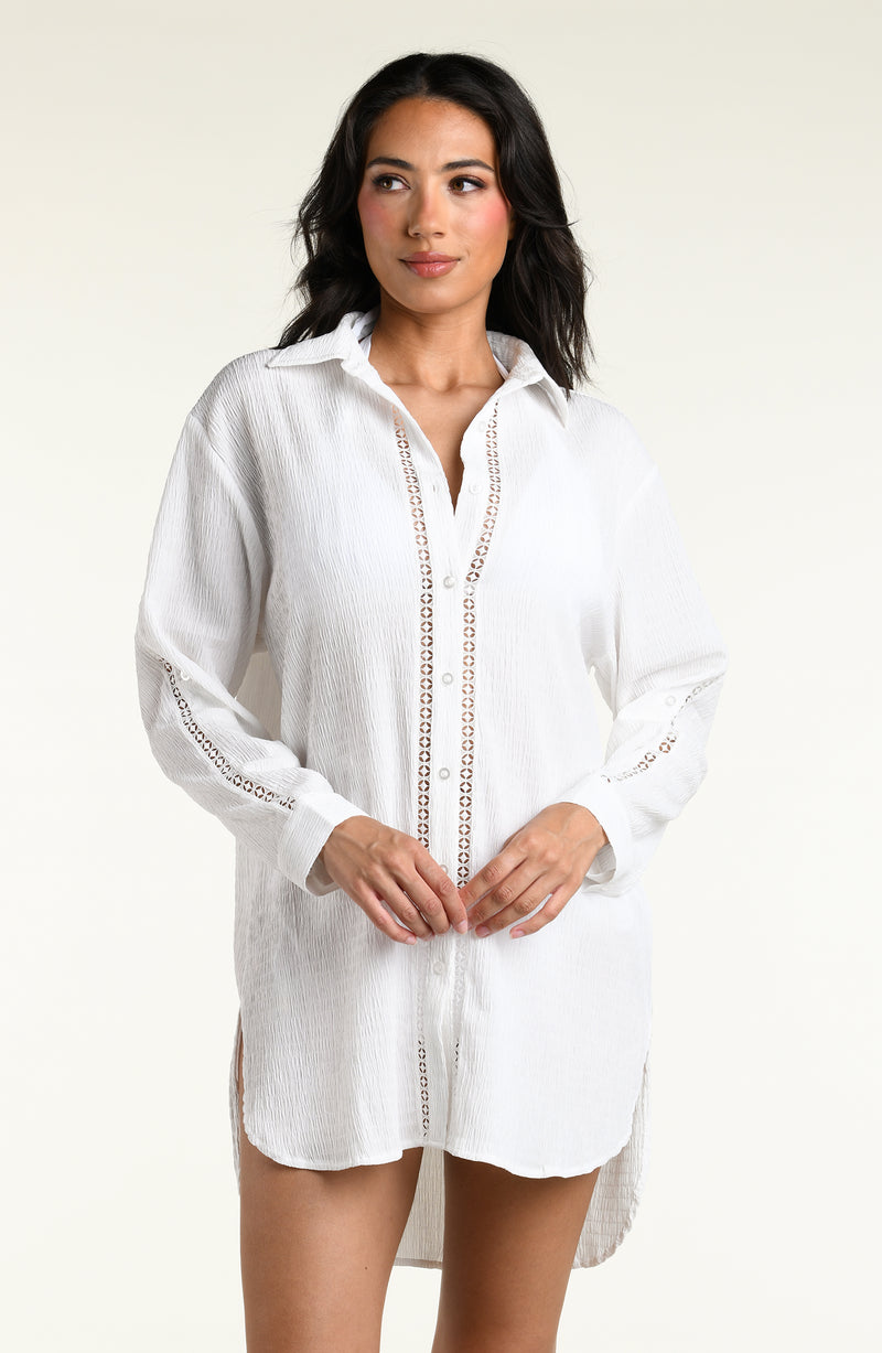 Woman wearing a white long sleeve cover up top against a white background. 