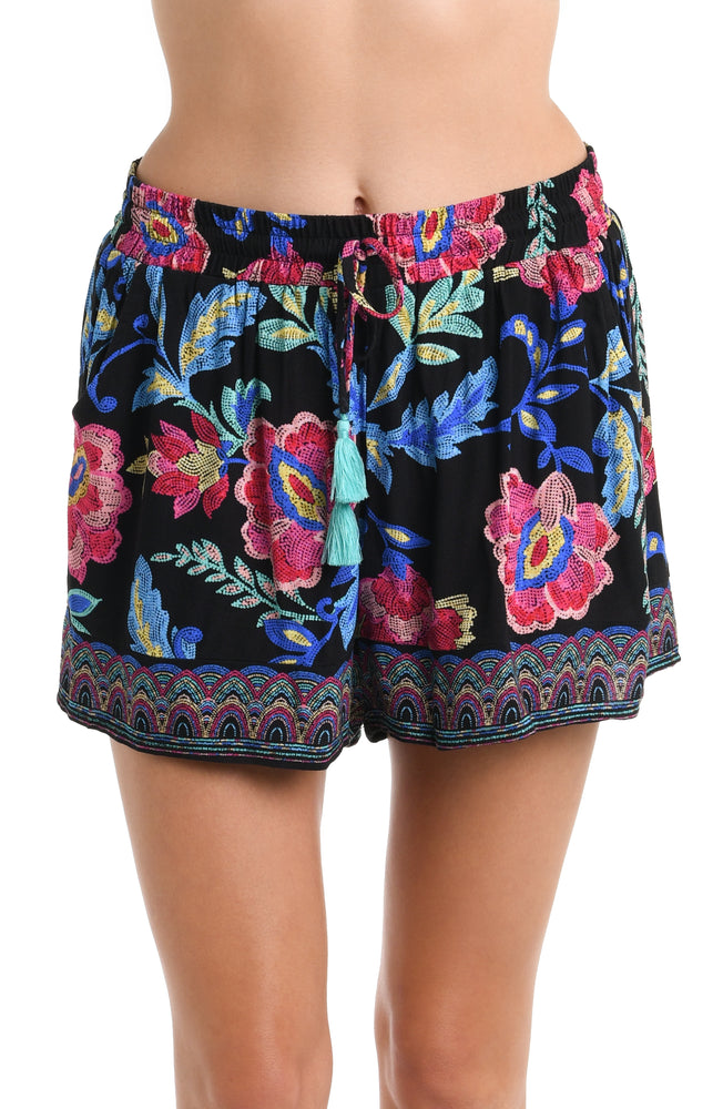 Model is wearing a black, pink, and blue multicolored floral patterned  Beach Shorts