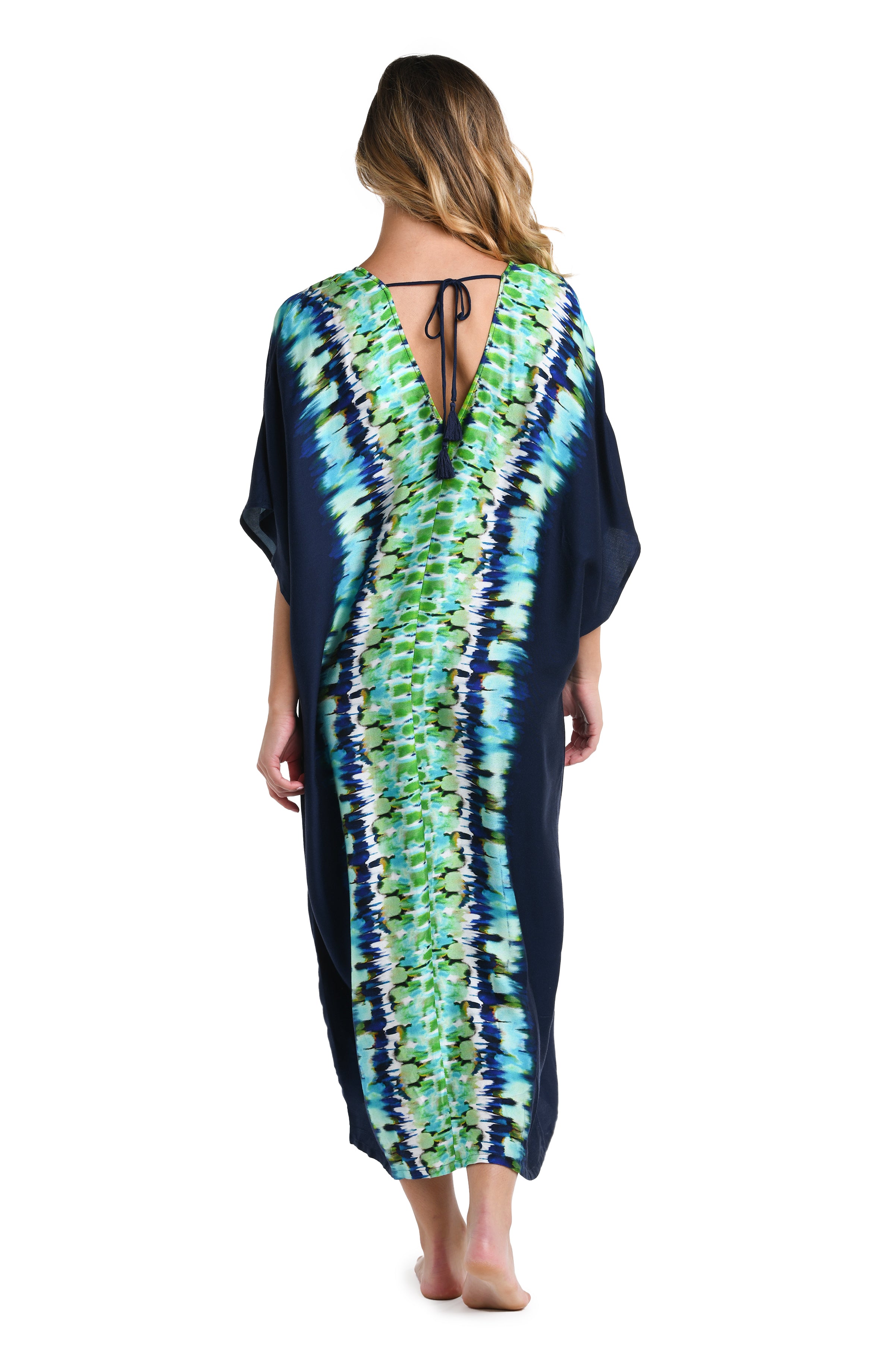 Full body back image of model wearing an indigo and blue tie-dye colored caftan cover-up featuring an adjustable neck tie, dolman sleeves, and a long cut.