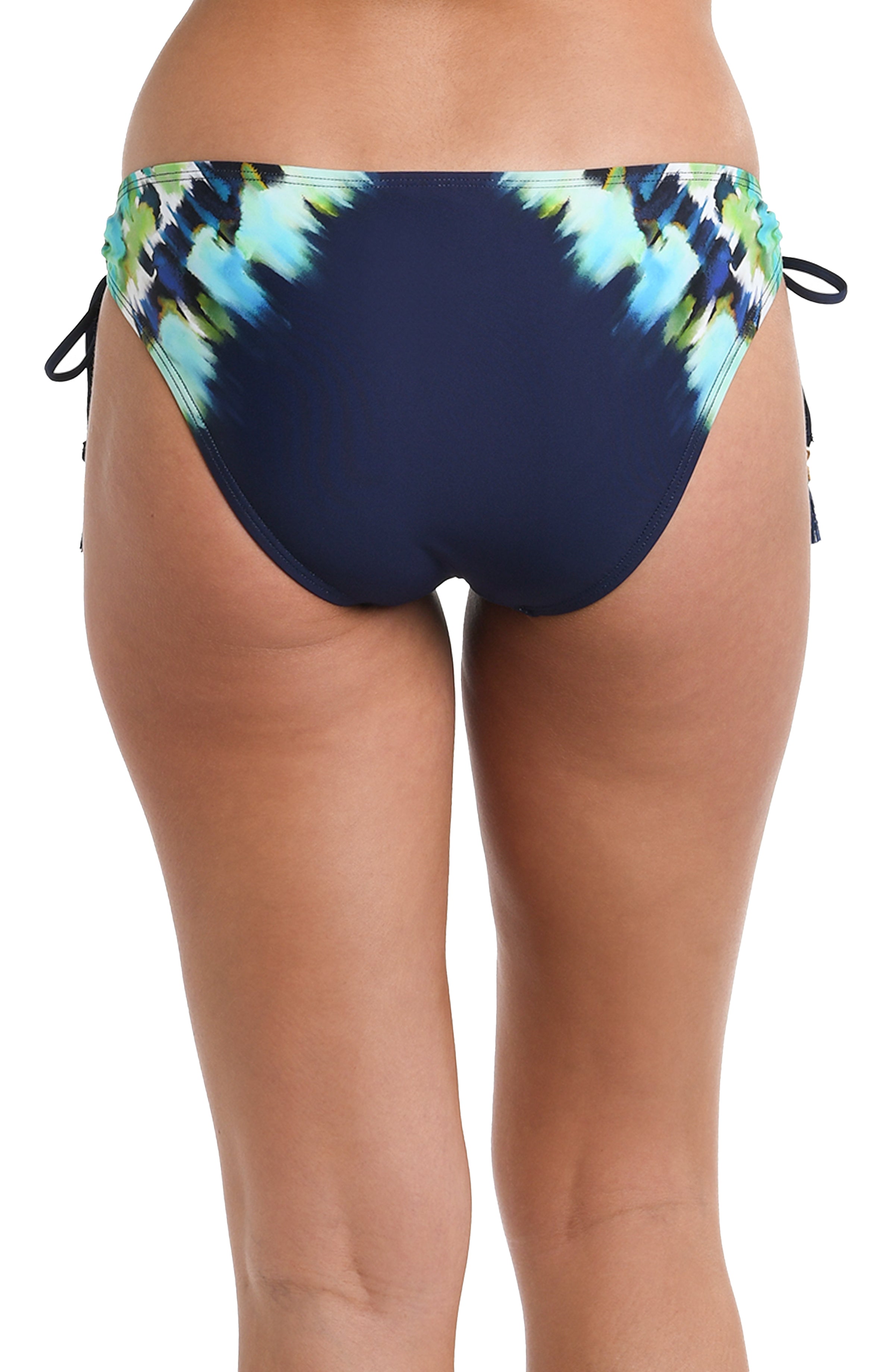 Back image of model wearing an indigo and blue tie-dye colored bikini swimsuit bottom featuring side ties adorned with tassels and moderate rear coverage.