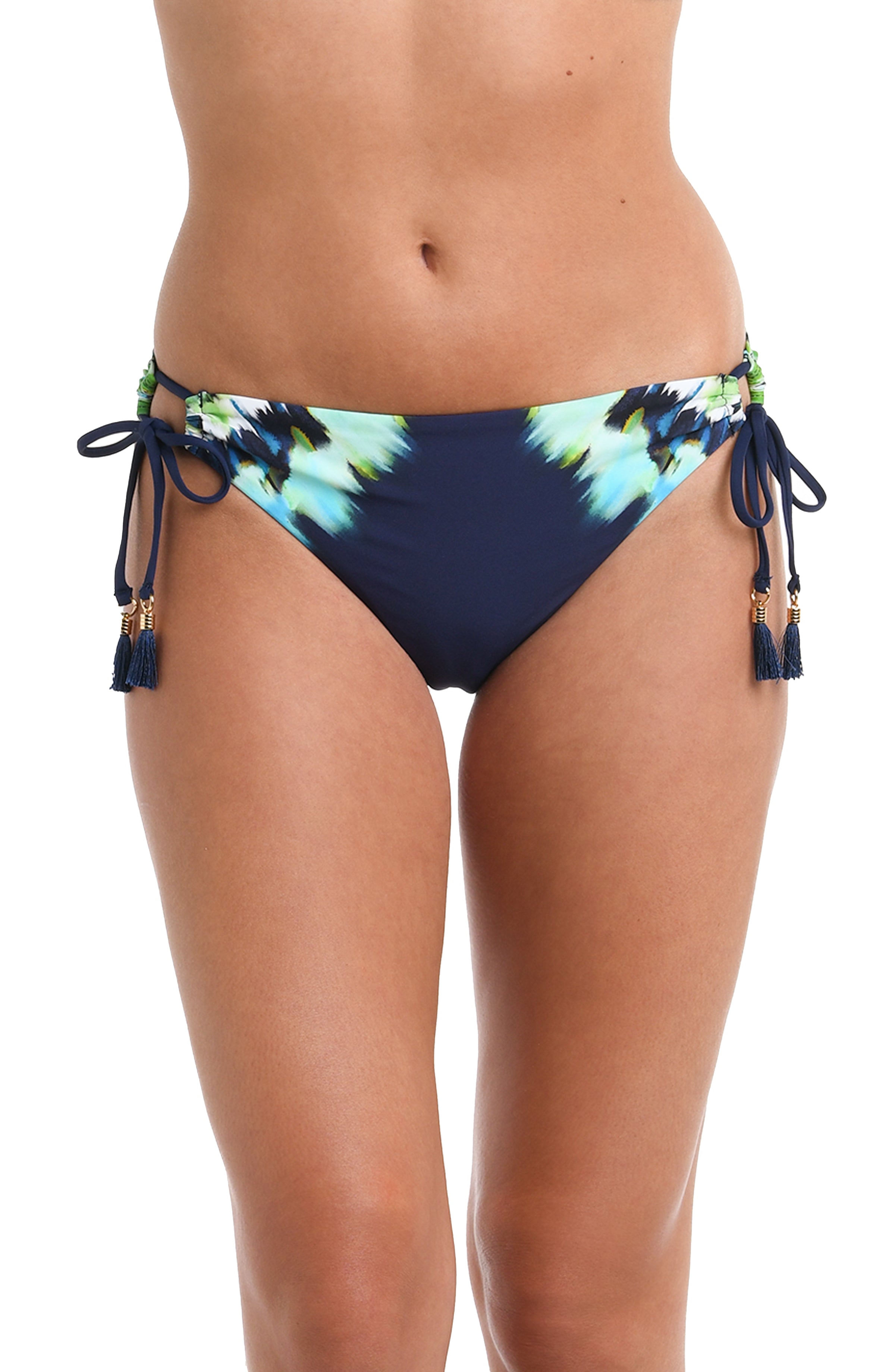 Front image of model wearing an indigo and blue tie-dye colored bikini swimsuit bottom featuring a hipster cut and side ties adorned with tassels.