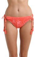 Front image of model wearing a coral colored palm printed bikini swimsuit bottom featuring a hipster cut and side ties adorned with tassels.