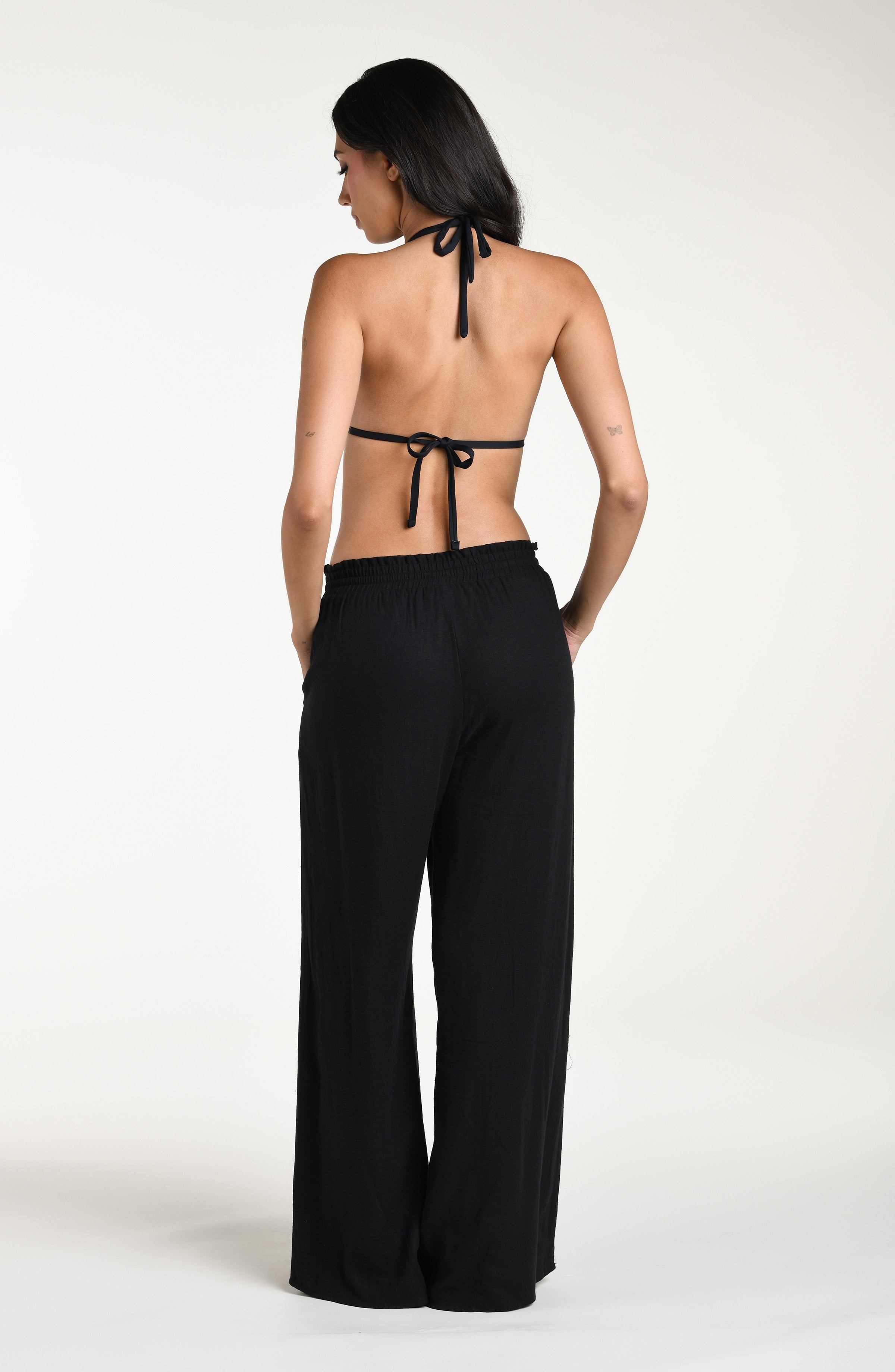 Woman wearing a black bikini top and wide-leg pants against a white background