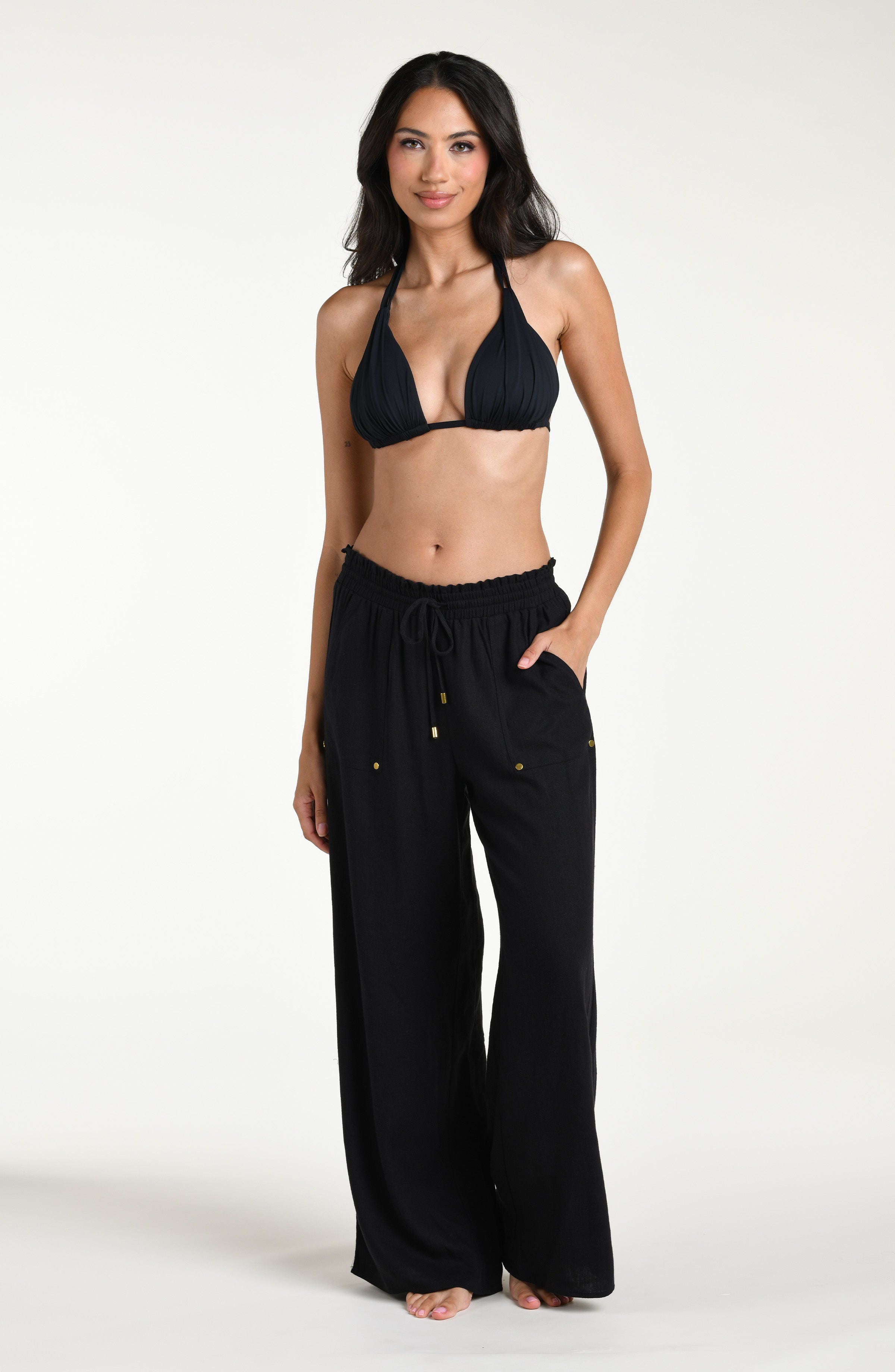 Woman wearing a black bikini top and wide-leg pants against a white background