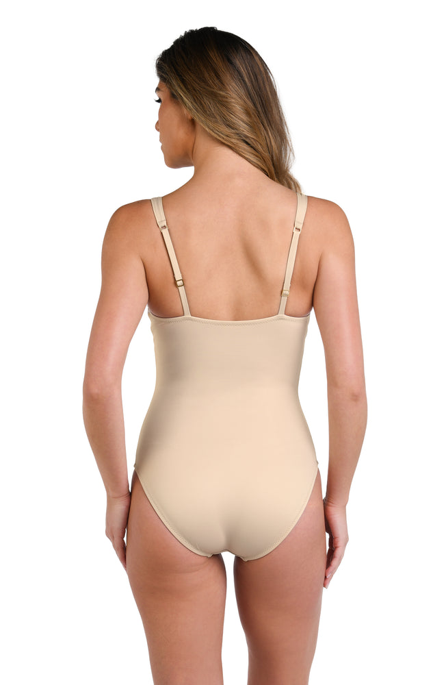 Model is wearing a solid taupe (sandy beige) colored plunge one piece swimsuit.