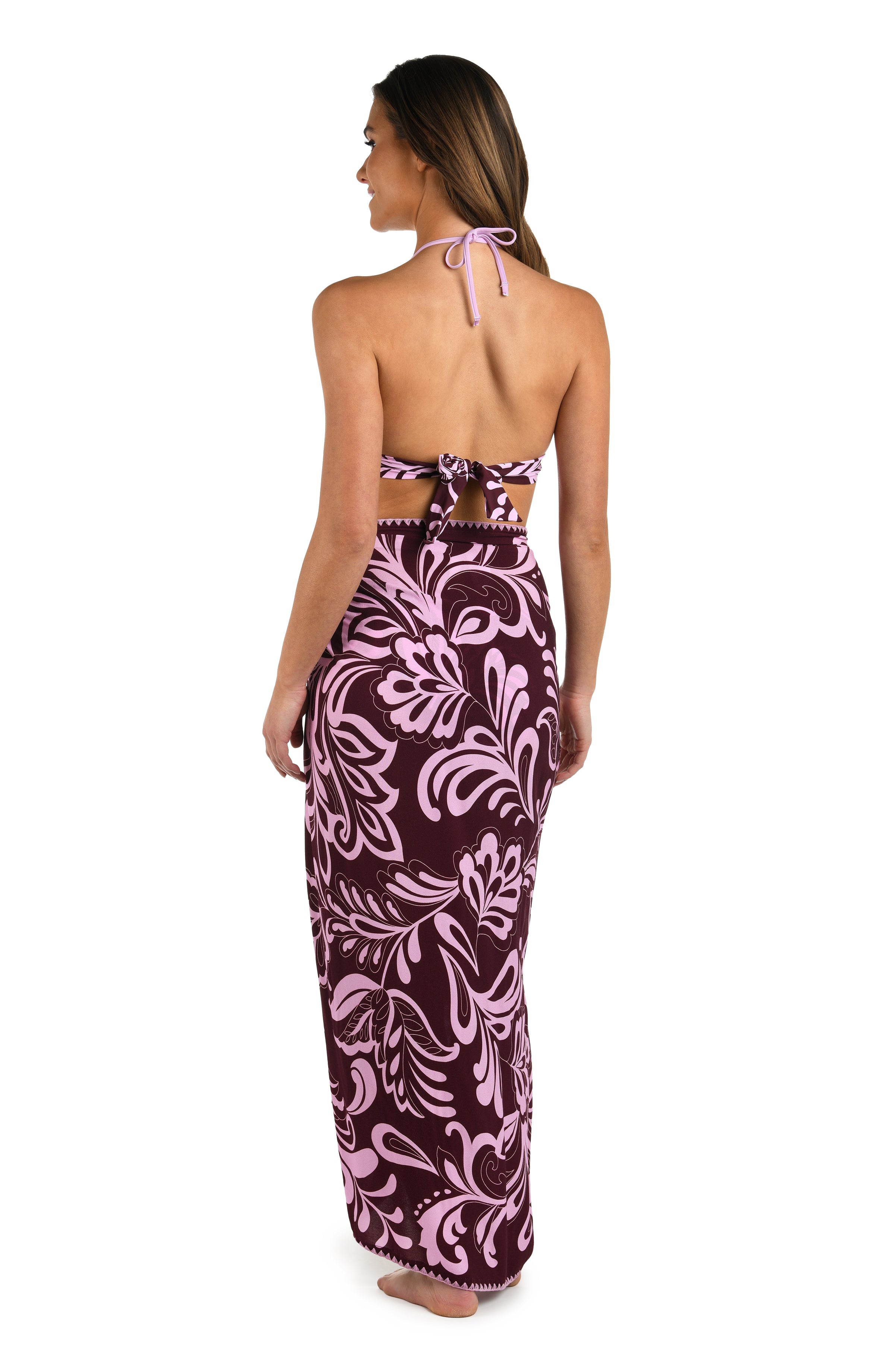 Full body back image of model wearing a dark cherry and pink tropical patterned pareo wrap cover up. 