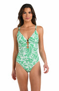 Front image of model wearing a green and white floral-printed one piece swimsuit featuring a plunge neckline, thin adjustable straps, triple keyhole cutouts, and a shirred body.