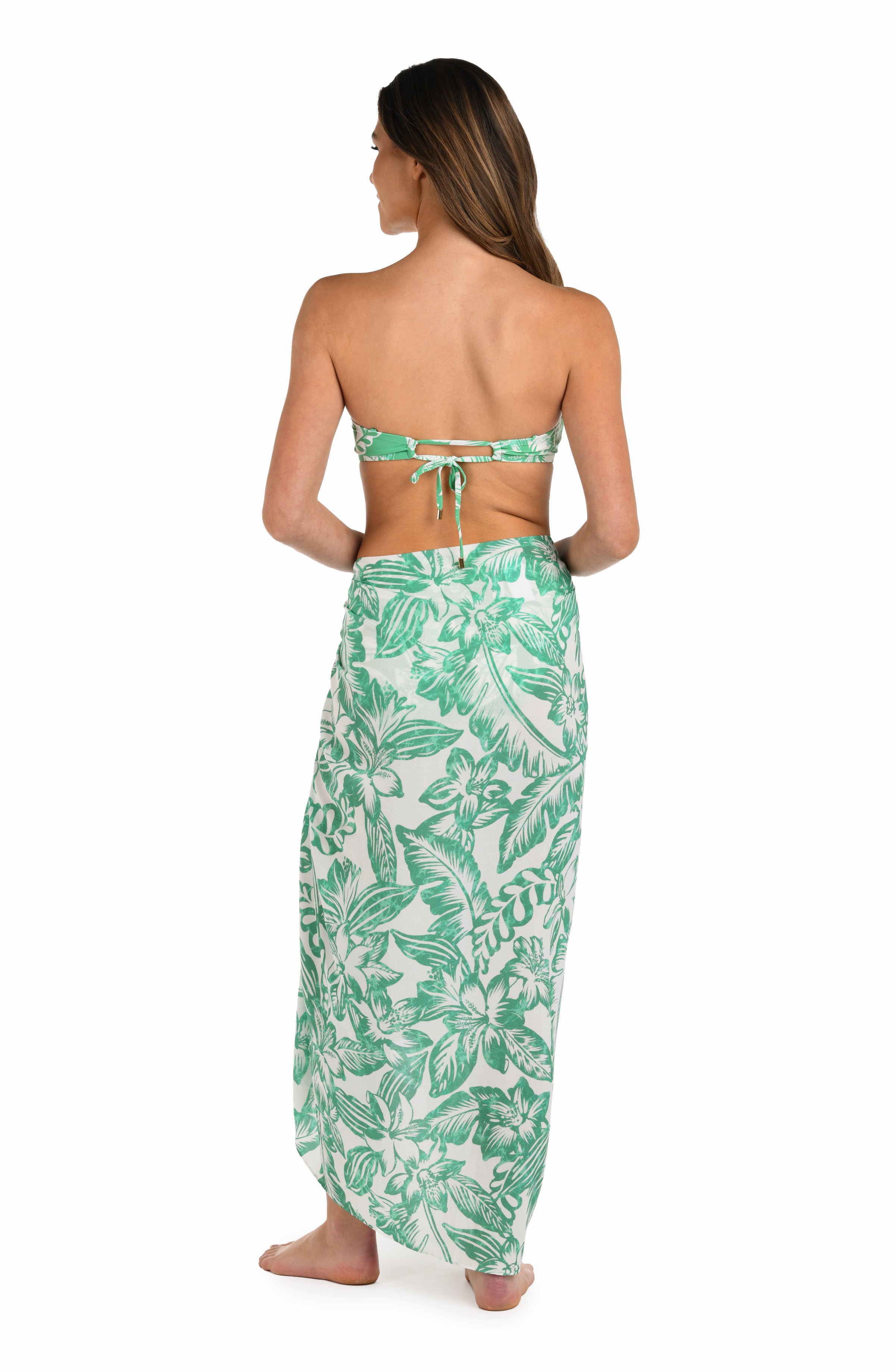 Full body back image of model wearing a green and white tropical-print pareo wrap cover up. 