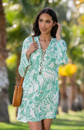 Lifestyle image of model wearing a green and white floral-printed long-sleeve tunic with a lace-up neckline and side pockets.